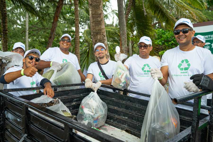 Strandreinigung mit Männern in weißen T-Shirts mit Recycling-Symbol, die Müll in Plastiksäcken sammeln.