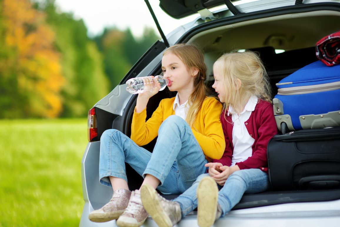 Two kids sitting in the car drinking from PET bottles