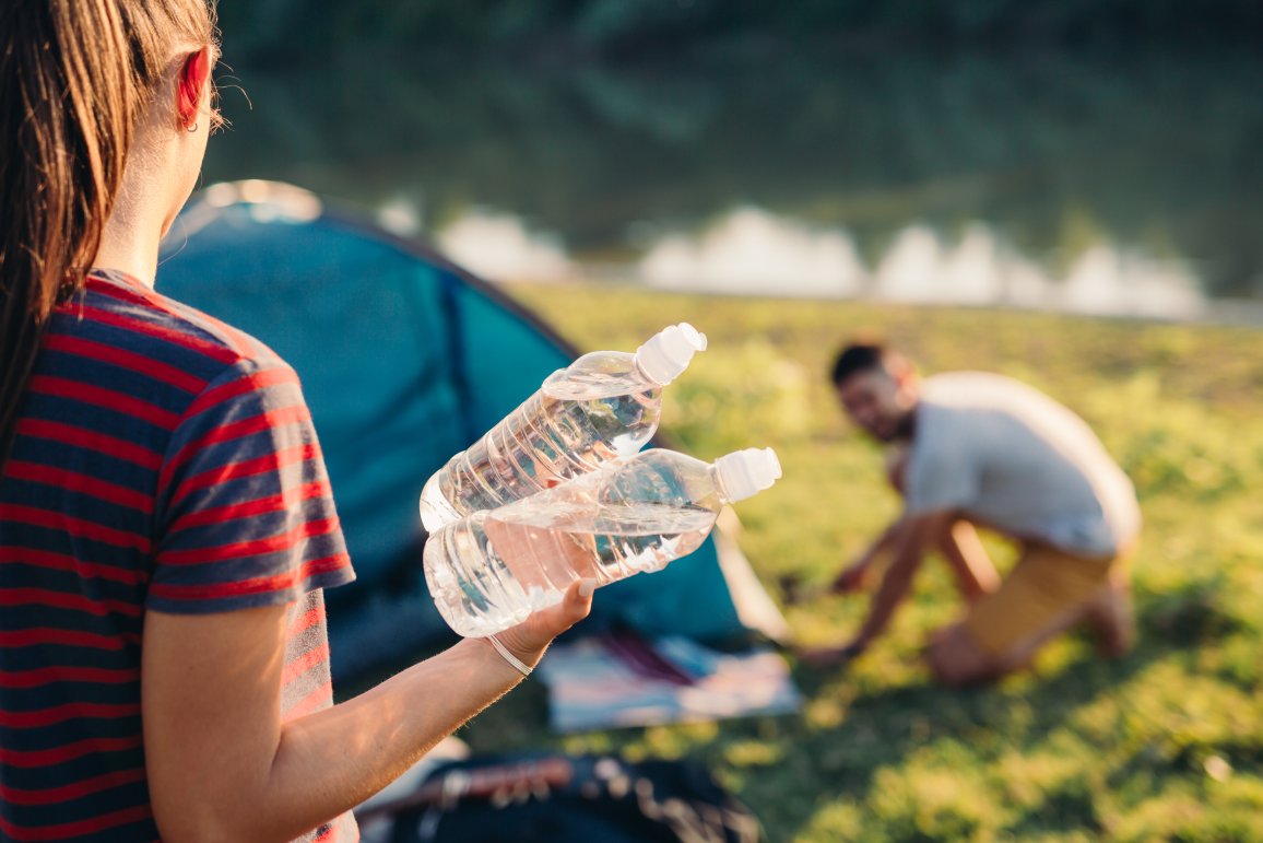 Picture shows camping situation. Women carries 2 PET bottles.