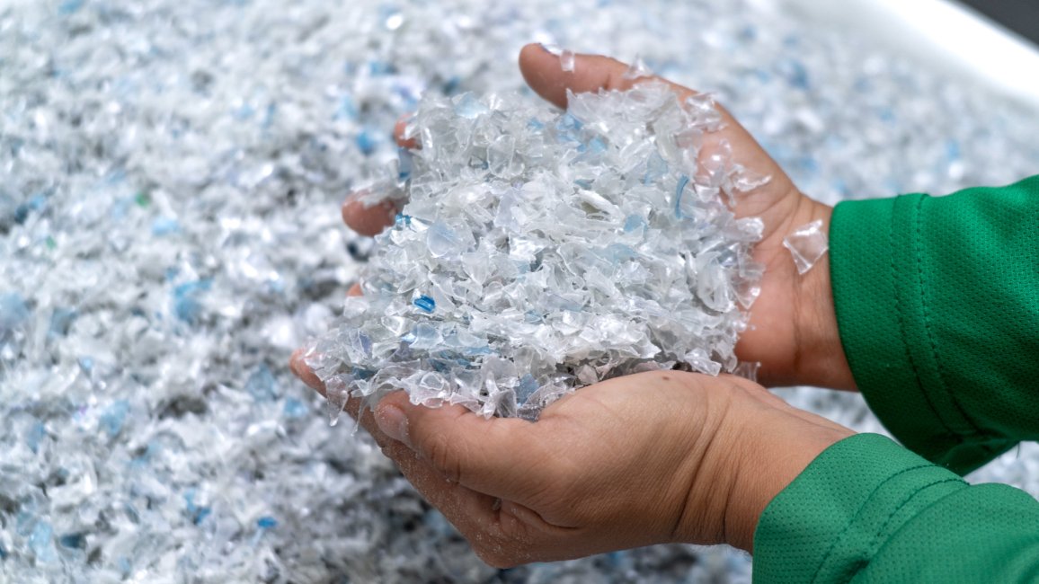 Hände, die recycelte Kunststoffflocken von ALPLA halten, um nachhaltige Verpackungsmaterialien zu präsentieren.