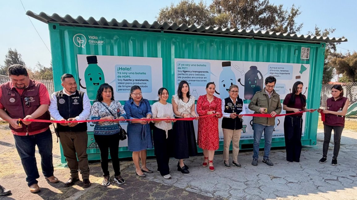 Eine Gruppe von Menschen schneidet ein rotes Band vor einem Recycling-Container durch.