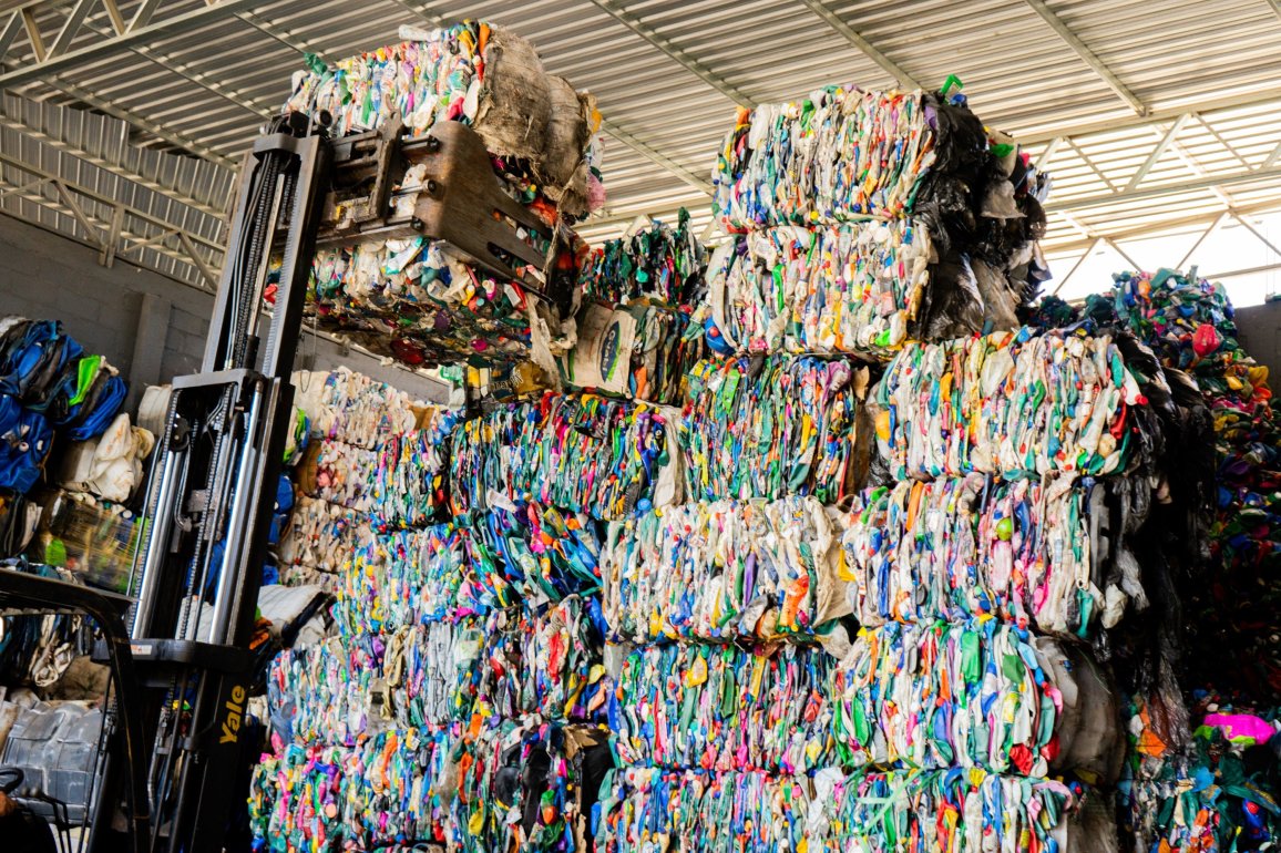 Ein Gabelstapler transportiert große Ballen aus gepressten Plastikflaschen in einer Recyclinganlage.