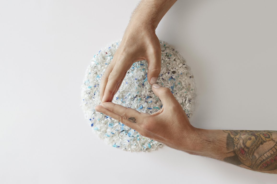 Hands forming a triangle shape over a pile of recycled plastic flakes.