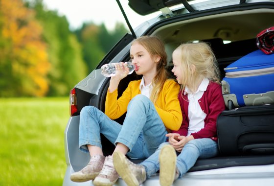 Two kids sitting in the car drinking from PET bottles