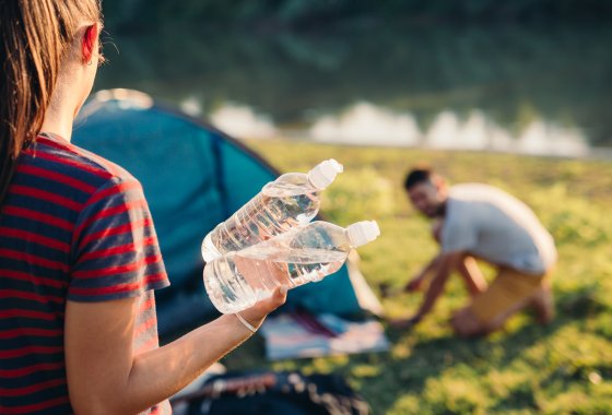 Picture shows camping situation. Women carries 2 PET bottles.