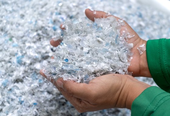 Hände, die recycelte Kunststoffflocken von ALPLA halten, um nachhaltige Verpackungsmaterialien zu präsentieren.