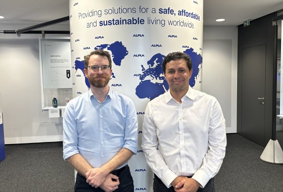 Two men in business attire standing in front of an ALPLA world map display.