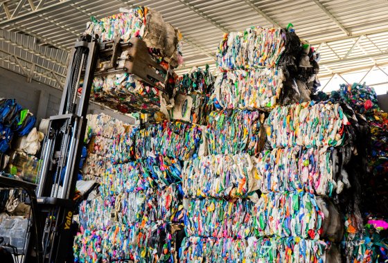 Forklift moving large bales of compressed plastic bottles in a recycling facility.
