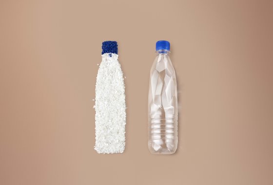 Plastic bottle filled with white resin pellets beside an empty clear plastic bottle, blue caps on both.