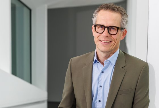 Georg Lässer, ein lächelnder Mann mit Brille und Sakko, der in einem hellen, modernen Büroflur steht.