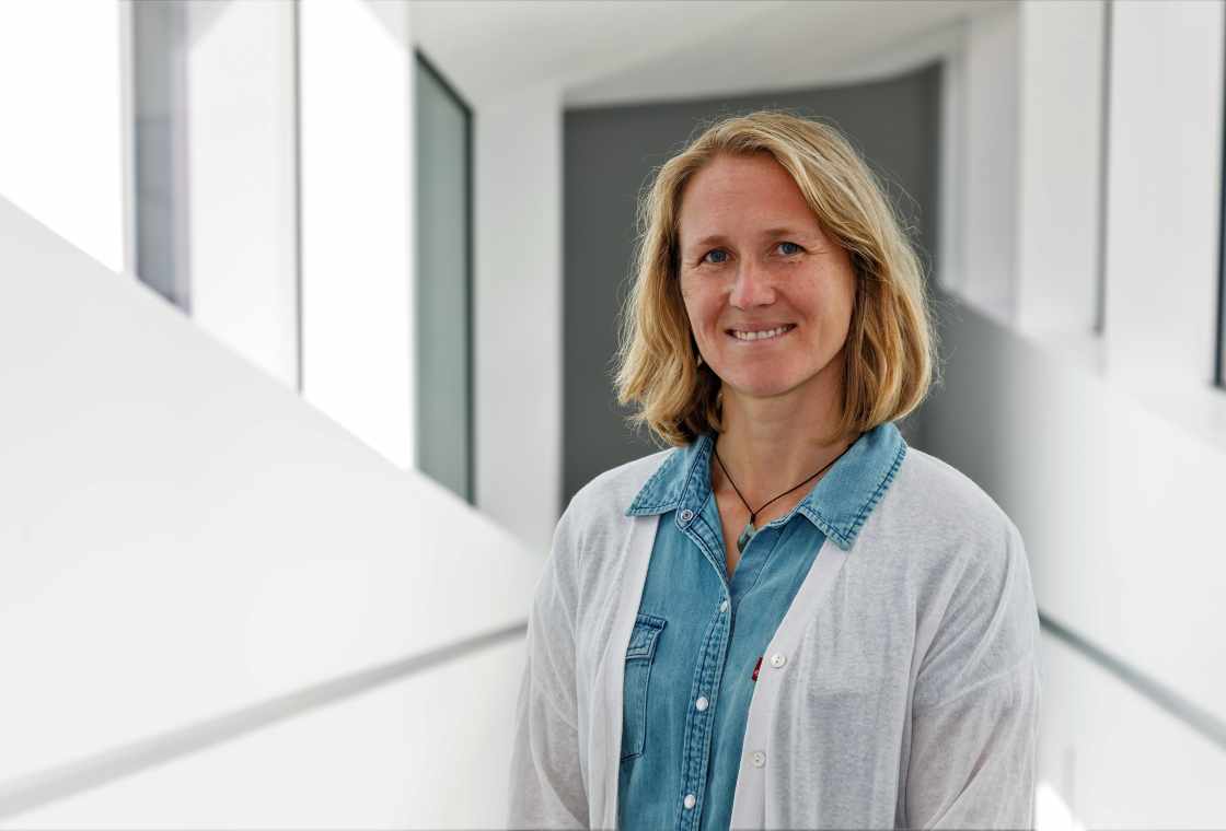 Porträt einer lächelnden Frau mit blonden Haaren und blauem Hemd in einem modernen Gebäude